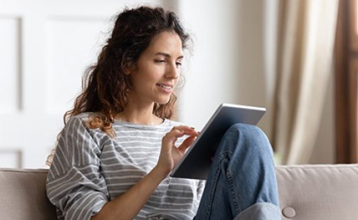 Smiling young woman using computer tablet, sitting on couch Smiling young woman using computer tablet, sitting on couch, typing on touchscreen, chatting in social network with friends, playing mobile device game or surfing internet, shopping online