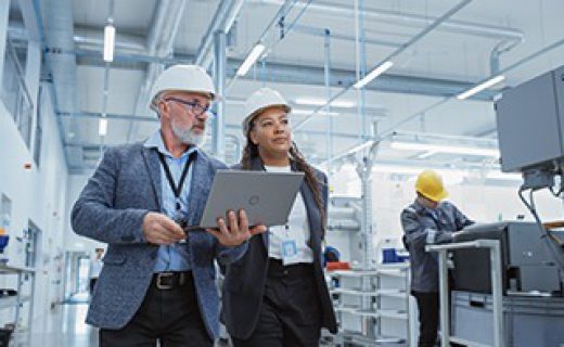 Two Professional Heavy Industry Engineers Wearing Hard Hats at Factory. Walking and Discussing Industrial Machine Facility, Working on Laptop. African American Manager and Technician at Work.